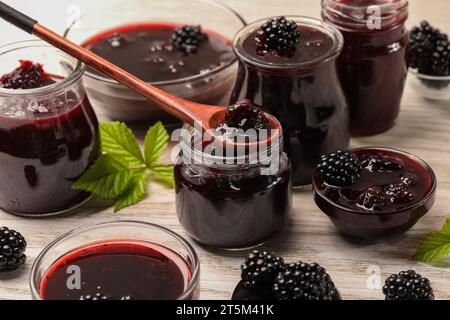 Prendre de la confiture de mûres savoureuse avec une cuillère sur une table en bois blanc Banque D'Images