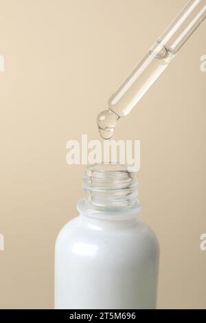 Goutte à goutte de sérum cosmétique de la pipette dans le flacon sur fond beige Banque D'Images