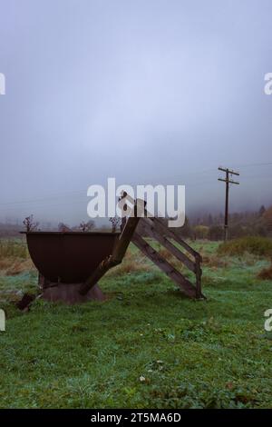 Salle de bain extérieure dans la cour arrière brumeuse. Baignoire en fer avec escaliers en bois sur le paysage d'automne. Vider la cuve rouillée en automne. Vacances à la campagne. Banque D'Images