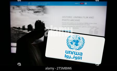 Personne tenant un smartphone avec le logo de l'agence des Nations Unies pour les réfugiés Plalestine UNRWA devant le site Web. Concentrez-vous sur l'affichage du téléphone. Banque D'Images