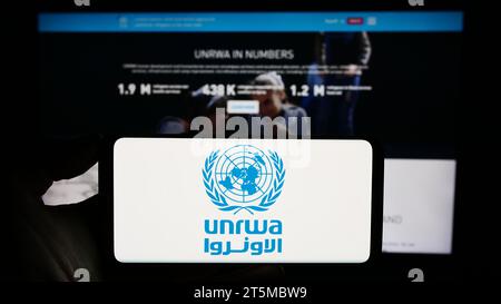 Personne tenant un téléphone portable avec le logo de l'agence des Nations Unies pour les réfugiés Plalestine UNRWA devant la page Web. Concentrez-vous sur l'affichage du téléphone. Banque D'Images