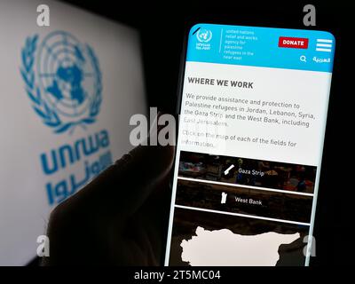 Personne tenant un téléphone portable avec la page Web de l'agence des Nations Unies pour les réfugiés Plalestine UNRWA devant le logo. Concentrez-vous sur le centre de l'écran du téléphone. Banque D'Images