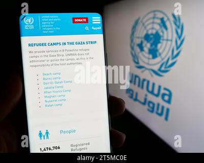 Personne tenant un smartphone avec la page Web de l'agence des Nations Unies pour les réfugiés Plalestine UNRWA devant le logo. Concentrez-vous sur le centre de l'écran du téléphone. Banque D'Images