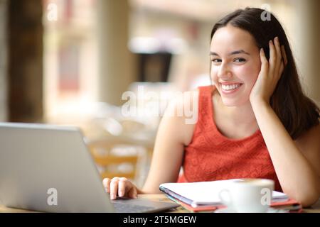 Étudiant heureux avec ordinateur portable et ordinateur portable vous regarde dans une terrasse de café Banque D'Images