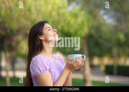 Profil d'une femme respirant buvant du café dans un parc verdoyant Banque D'Images