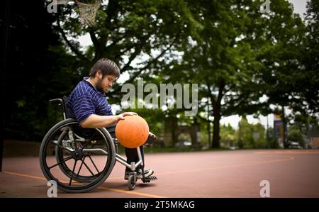 Un garçon pratique le basket-ball dans son fauteuil roulant dans un Laurelhurst Park à Portland, Oregon. Banque D'Images