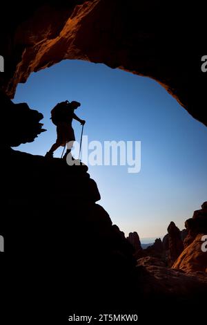 Randonneur se tenant debout sous une arche rocheuse naturelle dans le parc national des Arches, Utah. Banque D'Images