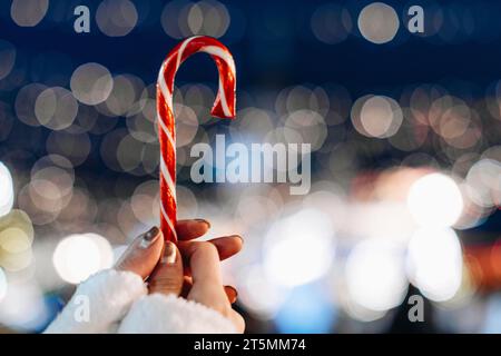 Mains femelles tenant rouge blanc canne sucrée lolipop sur le fond de bleu argent magie illumination.Détails de la fée de Noël Banque D'Images