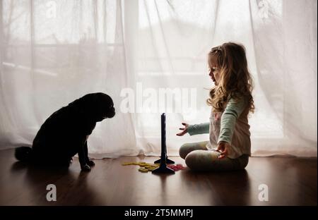 Petite fille jouant à un jeu de société avec un chiot noir Banque D'Images