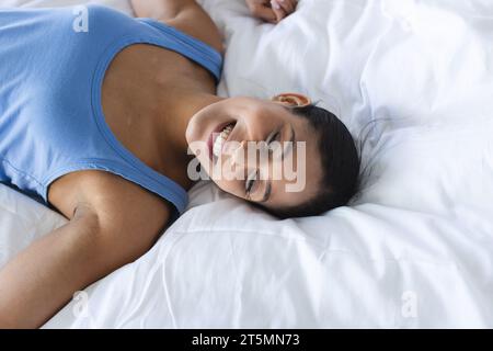 Heureuse femme biraciale portant un pyjama bleu et couchée dans la chambre Banque D'Images