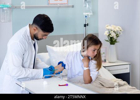 Médecin masculin diversifié ciblé prenant l'échantillon de sang avec la seringue de la patiente fille dans le lit d'hôpital Banque D'Images