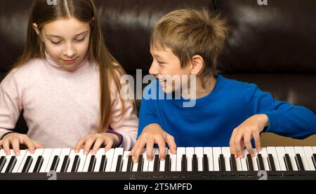 Heureux frère et sœur jouant du piano ensemble, partageant un moment joyeux Banque D'Images