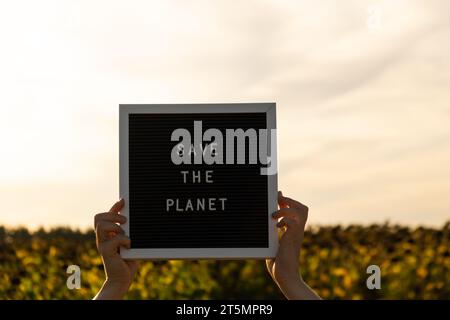 Les mains du manifestant avec du texte SAUVENT LA PLANÈTE sur le tableau noir sur fond de champ de tournesol. Réutilisation réduire le concept de recyclage. Protester pour la nature grève climatique manifestation volontaire contre la pollution terrestre, le réchauffement climatique Banque D'Images