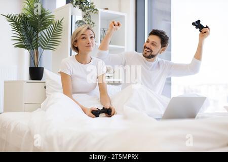 Couple caucasien dans l'amour amusez-vous en compétition dans le jeu d'ordinateur portable en utilisant des joysticks Banque D'Images