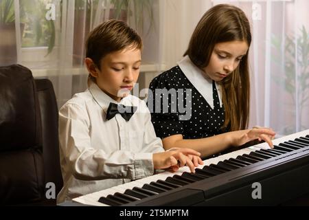 Un garçon et une fille, habillés intelligemment, partagent un moment de pratique musicale sur un piano à domicile. Banque D'Images