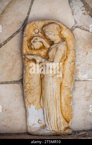 plaque ou panneau en pierre représentant la sculpture d'une femme grecque classique portant des vêtements traditionnels versant de l'eau d'une cruche dans sa main Banque D'Images