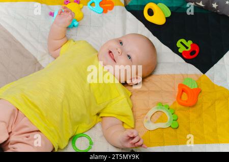 Mignon petit bébé nouveau-né entouré de jouets colorés, allongé à la maison sur le lit Banque D'Images