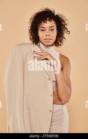 femme afro-américaine à la mode posant en blazer d'automne et mini robe sur fond beige Banque D'Images