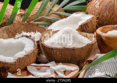 Noix de coco fraîches ouvertes avec des tranches de noix de coco, des flocons et des feuilles de noix de coco sur une table en bois. Joli fond de fruits pour vos projets. Banque D'Images