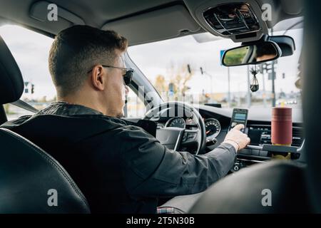 Un homme utilise un smartphone installé dans le support tout en conduisant une voiture. Banque D'Images