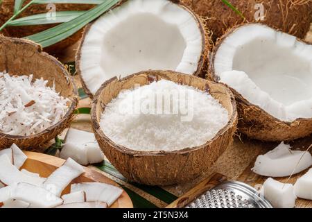 Noix de coco fraîches ouvertes avec des tranches de noix de coco, des flocons et des feuilles de noix de coco sur une table en bois. Joli fond de fruits pour vos projets. Banque D'Images