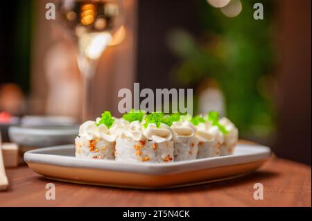 Rouleau de sushi avec fromage à la crème, graines de sésame et caviar de poisson volant vert sur une assiette en gros plan. Photo de haute qualité Banque D'Images