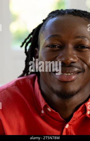 Portrait de l'homme afro-américain heureux avec des dreadlocks souriant dans la chambre ensoleillée Banque D'Images