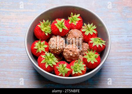 Un bol de grappes rondes de noix de chocolat avec des fraises fraîches entourant les boules de chocolat qui sont placées au centre du bol Banque D'Images