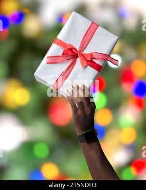 Gros plan de la main masculine soulevant le cadeau de Noël avec le fond de l'arbre de Noël Banque D'Images