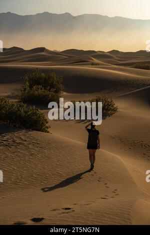Une personne solitaire marchant dans le désert de la Vallée de la mort, près de Mesquite Flats, Californie, au lever du soleil. Lumière vive et ciel brumeux. Banque D'Images