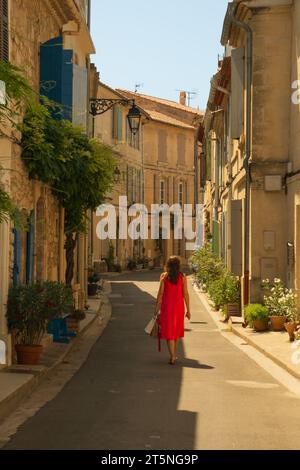 Femme dans une belle robe rouge marchant dans la ville historique du sud d'Arles, le sud de la France.maisons en briques typiques et ciel bleu vif. Banque D'Images