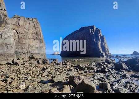 plage rocheuse avec une grande formation rocheuse dentelée sous un ciel bleu clair, avec de petits rochers et des rochers dispersés autour Banque D'Images