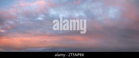 ciel panoramique au coucher du soleil, où les couleurs vibrantes du coucher du soleil se reflètent dans les nuages doux et ondulants. Cette image fascinante capture le crépuscule serein Banque D'Images