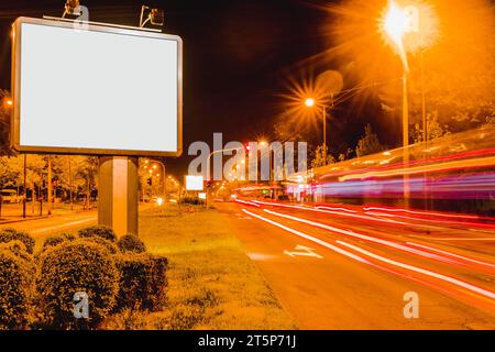 Panneau d'affichage blanc près du bord de la route avec des sentiers de feux de circulation aux heures de pointe Banque D'Images