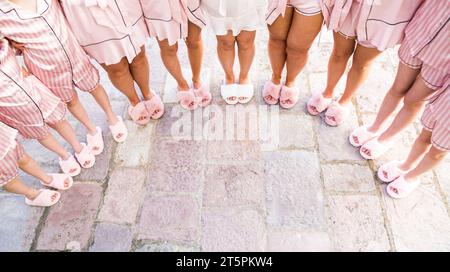 Mariée et demoiselles d'honneur se tiennent en pyjama et pantoufles sur les carreaux en demi-cercle. Rogné. Sans visage Banque D'Images