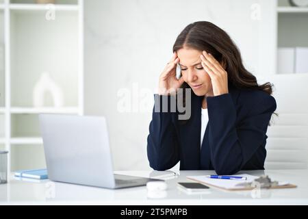 Femme d'affaires mature stressée assise sur le lieu de travail, souffrant de maux de tête Banque D'Images