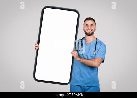 Docteur homme tenant le grand téléphone avec l'écran blanc pour l'annonce médicale, maquette Banque D'Images