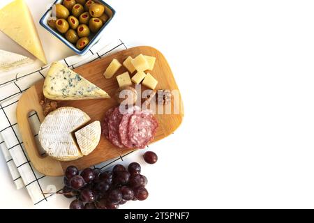 Différents types de fromages avec raisin, olives et noix sur fond blanc Banque D'Images