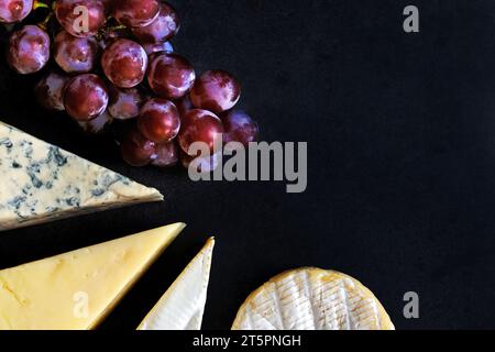 Différents types de fromages avec raisin sur fond noir Banque D'Images