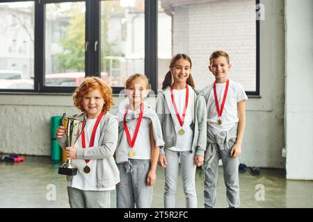 gai petites filles et garçons souriant et posant avec trophée et médaille d'or, sport pour enfants Banque D'Images