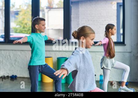 joyeux trois enfants en vêtements de sport faisant des exercices d'étirement avec les mains asides, sport pour enfants Banque D'Images