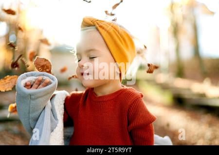 Petite fille aux yeux fermés met son manteau sous les feuilles tombantes dans la forêt Banque D'Images