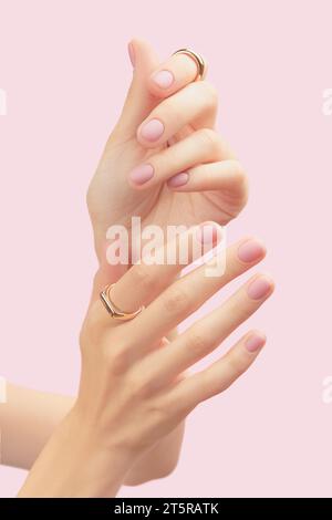 Belles mains de femmes soignées avec un design d'ongle rose mat sur un fond rose Banque D'Images