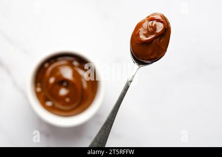 Une cuillerée et un bol plein de dulce de leche sur fond de marbre blanc avec espace de copie. Banque D'Images