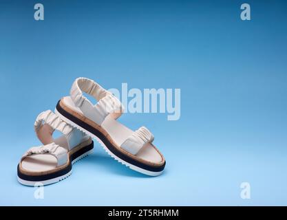 Un cliché de nouvelles sandales en cuir pastel avec semelles tricolores placées les unes sur les autres. Fond bleu dégradé. Concept de vente de chaussures Banque D'Images