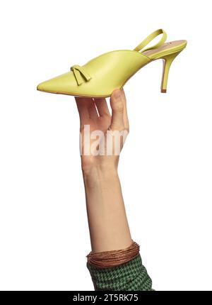 Une main de femme avec des bracelets brillants tenant une élégante chaussure d'été à talons hauts vert citron à bout pointu isolée sur un fond blanc. Pied tendance Banque D'Images