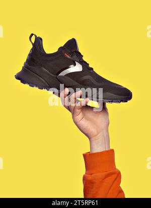 Présentation élégante de sneaker noire dans la main d'un homme, isolé sur un fond jaune. Vendre des chaussures de sport modernes. Concept publicitaire Banque D'Images