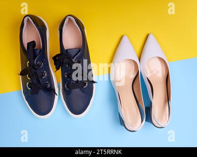 Deux paires de chaussures modernes féminines : escarpins blancs ouverts à dos ouvert avec des talons évasés noirs et des sneakers bleu marine décontractées sur fond bleu-jaune. Vue de dessus, cl Banque D'Images