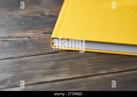 Une image recadrée d'un livre épais avec une couverture rigide texturée jaune isolée sur un bureau en bois avec un espace de copie pour le texte. Modèle pour photographes ou desi Banque D'Images