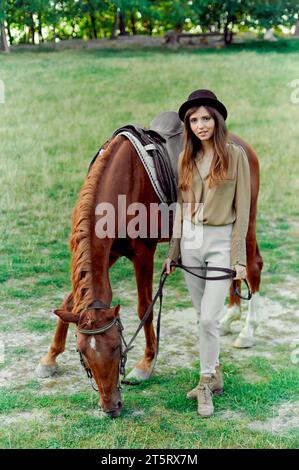 Jeune femme en chapeau noir avec cheval brun à la campagne. L'équitation favorise le bien-être, la relaxation. certificat cadeau pour émotion, type de therapeu Banque D'Images